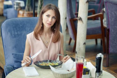 Pembe elbiseli çekici gülümseyen genç kadın bir restoranda öğle yemeği var. Masada makarna ve içeceklerin olduğu bir tabak.
