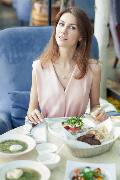 Potret wanita muda cantik dengan gaun merah muda memiliki makan siang di sebuah restoran. Makanan dan minuman di atas meja . — Stok Foto