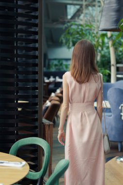 bir restoranda uzun koyu saçlı uzun pembe elbiseli ince bir kızın arkasından görünümü. Kadın taşınıyor.