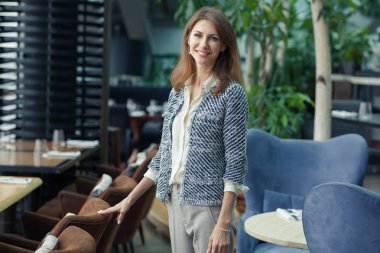 zarif gri pantsuit ve beyaz gömlek güzel genç gülümseyen iş esmer kadın bir kafede duruyor