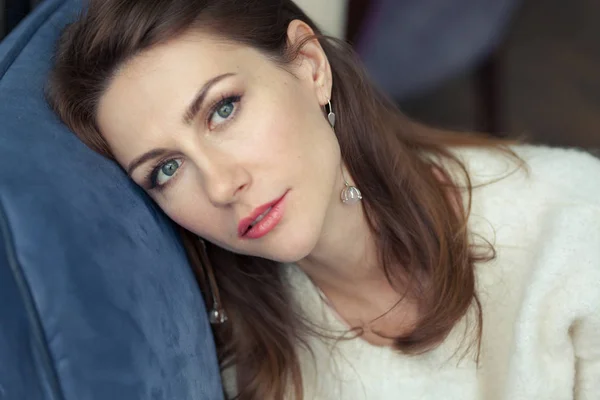 Rahat yumuşak beyaz kazak çekici dalgın genç kadın esmer yakın çekim yüz portresi. Kız mavi koltukta oturur