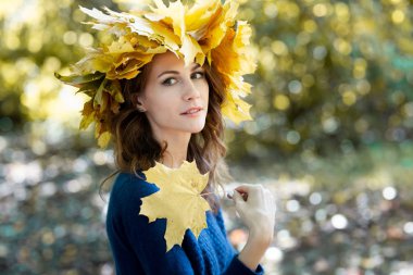 Başında sarı akçaağaç yaprakları bir çelenk ve mavi mayo ile güzel bir genç esmer kadının yakın çekim portre. kız elinde sonbahar akçaağaç yaprakları tutar. Arka planda Altın park.