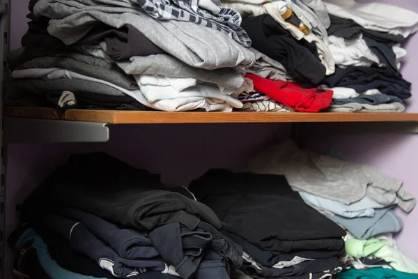 Stapels van niet netjes gevouwen kleding van verschillende kleuren op een houten plank — Stockfoto