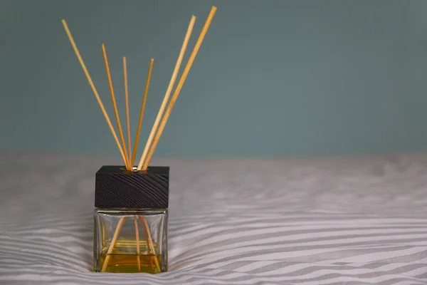 Un difusor de vidrio con una cubierta de madera negra, palos de madera y soporte de aceite aromático amarillo sobre una colcha gris. pared gris-azul en el fondo. enfoque selectivo — Foto de Stock