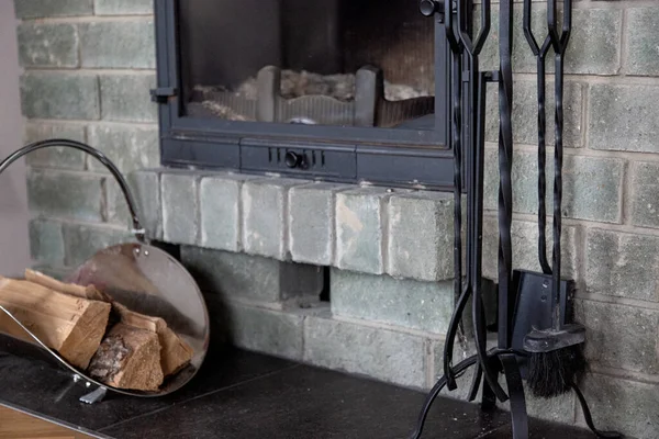 close-up gray brick wall fireplace. cast-iron fireplace accessories and firewood in a metal basket nearby.