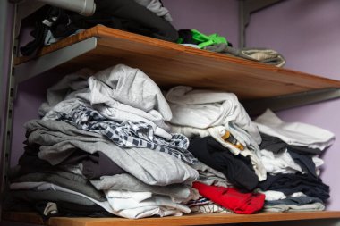 Ahşap bir rafta düzgünce katlanmamış farklı renkte giysiler yığını