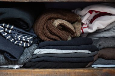 Ahşap bir rafta yığılmış farklı renkte kıyafetlerin yakın çekimi.