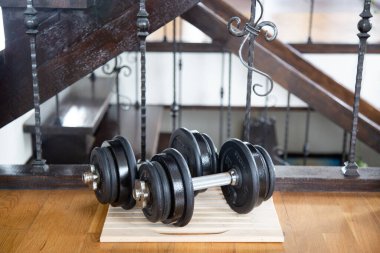 Ahşap zemin üzerinde diskleri olan iki siyah spor salonu dambılı. Evde spor.