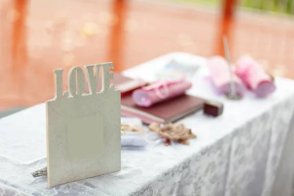 white photo frame with the word Love and other wedding attributes on a white table of a wedding registration ceremony outside