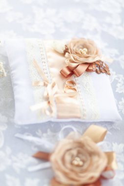 Dantelle süslenmiş beyaz bir yüzük yastığının üzerinde iki altın alyans ve kurdelelerden yapılmış bej bir gül var. Seçici odak