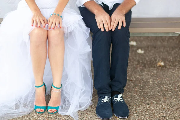 Jambes de la mariée dans une robe blanche et le marié assis sur le banc. Les paumes des jeunes mariés reposent sur leurs genoux. Pas de visage — Photo