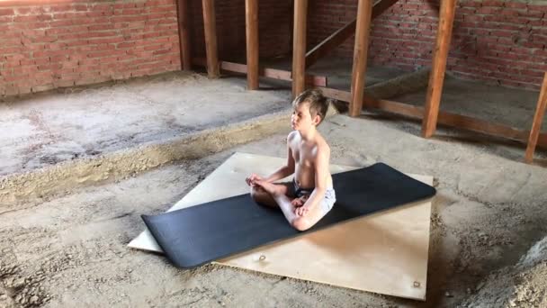Мальчик медитирует на коврике для йоги на фоне чердака . — стоковое видео