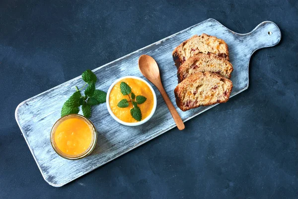 Ahşap tahtada meyveli ekmek ve mavi arka planda kaşıkla reçel.