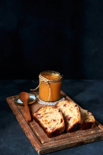 Ahşap tahtada meyveli ekmek ve mavi arka planda kaşıkla reçel.