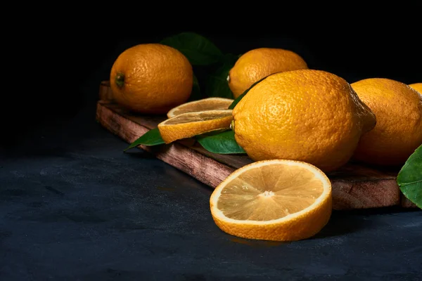 Koyu mavi arka planda yaprakları olan ahşap bir tahtanın üzerinde dilimlenmiş limonlar.