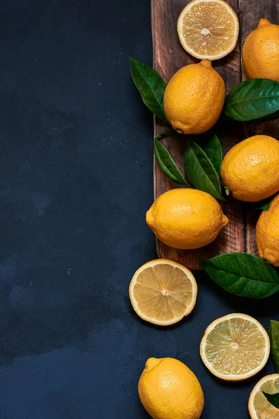 Koyu mavi arka planda yaprakları olan ahşap bir tahtanın üzerinde dilimlenmiş limonlar.