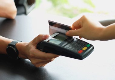 Dükkandaki ürünleri müşterilere satmak için kredi kartı okutma makinesi kullanan bir adam. Kredi kartıyla harcama kavramı.