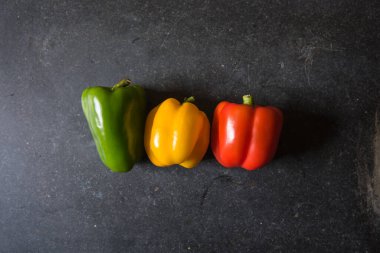 Siyah arka planda kırmızı sarı ve yeşil dolmalık biberlerin üst görüntüsü