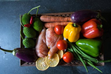 Taze sebzeler ve arka plandaki tepside servis edilen çiğ tavuk eti.
