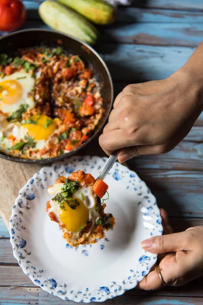 Orta doğu yemeğinin bir kısmını servis eden bir el, Shakshouka 'yı tavadan beyaz bir tabağa servis ediyor.