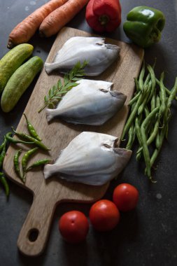Tahtadaki çiğ balık ve taze sebzelerin dikey görüntüsü