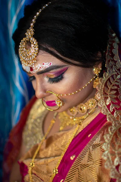 Portrait of a cute Indian model in Bridal look with heavy gold jewelry and red sari