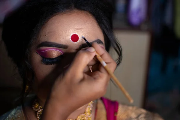 a makeup artist drawing a beautiful design called kolka or Bindi in India on the forehead of a bride