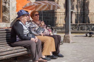 Potes, Cantabria, İspanya; 18 03: 2017: 3 yaşlı kadın bir bankta oturan şapka, güneş gözlüğü ve şemsiyeyle gülümsüyor