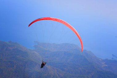 Paragliding. Paraglider dağların üzerinden uçuyor. Mavi gökyüzünde ve deniz arka planında paragliding yapıyor..