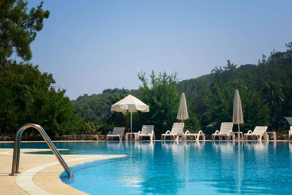 Beyaz şemsiyeler ve havuz kenarında güneşlenirler.