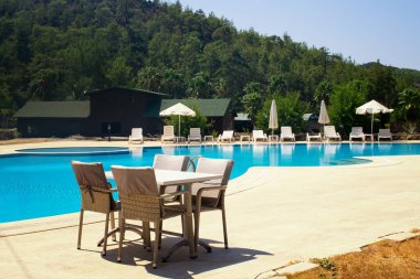 Beyaz şemsiyeler ve havuz kenarında güneşlenirler.