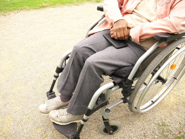 Nahaufnahme des Körpers einer älteren behinderten schwarzen Frau im Rollstuhl, die ihr Handy an den Beinen hält — Stockfoto