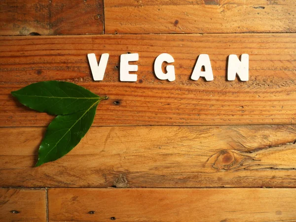 VEGAN kelimesi beyaz harflerle tahta arka planda iki defne yaprağı ile.