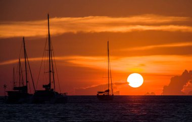 Nai Harn Sahili, Phuket, Tayland 'da bir körfezde portakal rengi günbatımı, yatlar ve katamaranların siluetleri.