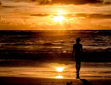 Bir kızın silueti Endonezya, Bali 'deki Dreamland Sahili' nde altın bir günbatımına gidiyor.