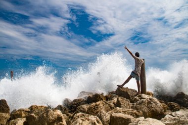 Endonezya 'nın Bali adasında, mavi gökyüzüne karşı büyük dalgalarla okyanusun kenarında duran adam.