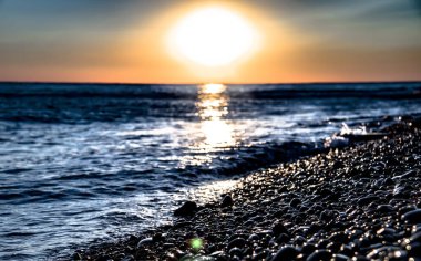 Rusya 'nın Anapa eyaletinin Bolshoy Utrish köyü yakınlarındaki bir çakıl taşı kıyısına güzel bir günbatımı yansıtılır.