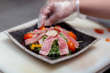 Şef, yemek hazırlamak için bir restoranda susam tohumları, domatesler ve otlar serpiştirilmiş balık parçalarıyla malzemeleri çok güzel bir şekilde bir restorana koyar.