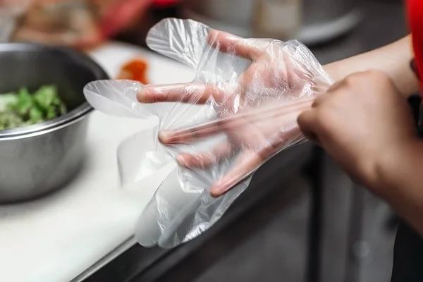 Şef yemek pişirmek için elini tek kullanımlık eldivenlere koyar.