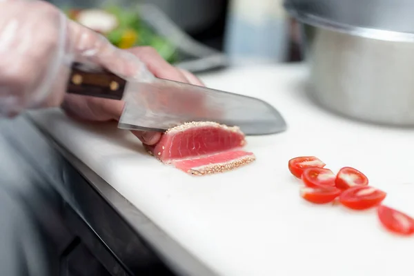 Şef, lokantada yemek hazırlamak için üzerine susam tohumu serpiştirilmiş keskin bir bıçakla güzelce keser.