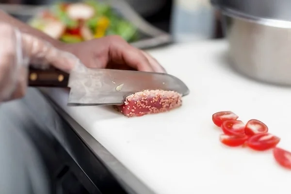 Şef, lokantada yemek hazırlamak için üzerine susam tohumu serpiştirilmiş keskin bir bıçakla güzelce keser.