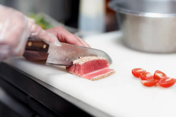 Şef, lokantada yemek hazırlamak için üzerine susam tohumu serpiştirilmiş keskin bir bıçakla güzelce keser.