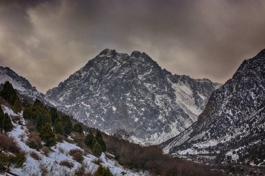 Kar, yatay, karanlık kayalık dağ ridge siluet sisli bulutlar ve orman şapkalı. Issyk-ata, Kırgızistan.