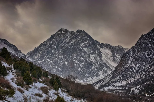 Kar, yatay, karanlık kayalık dağ ridge siluet sisli bulutlar ve orman şapkalı. Issyk-ata, Kırgızistan.