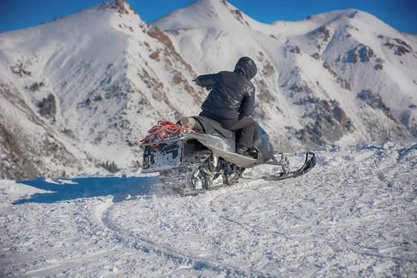 Rider on the snowmobile in the mountains ski resort. Winter snow landscape. Riding with fast turn.