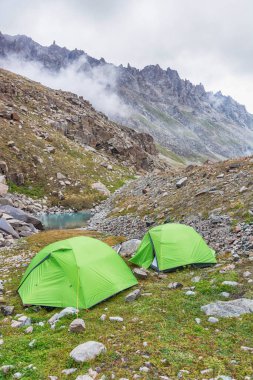 Göl kenarında iki yeşil çadır ve dağlarda bulutlar. Kırgız Alatoo Dağları, Tian-Shan, Ala-archa, Kırgızistan.