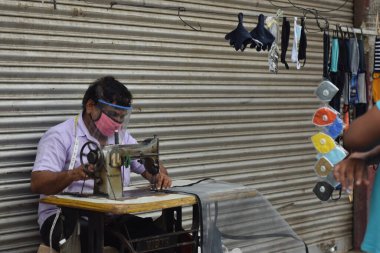 Hyderabad, Telangana, Hindistan. Temmuz-19-2020: terzi koruyucu yüz maskesi takarken giysileri tamir etmek, dikmek ve ayarlamak içindir. Yüzünde güvenlik maskesi olan bir adam, salgın konsepti.