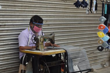 Hyderabad, Telangana, Hindistan. Temmuz-19-2020: terzi koruyucu yüz maskesi takarken giysileri tamir etmek, dikmek ve ayarlamak içindir. Yüzünde güvenlik maskesi olan bir adam, salgın konsepti.