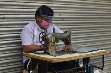 Hyderabad, Telangana, Hindistan. Temmuz-19-2020: terzi koruyucu yüz maskesi takarken giysileri tamir etmek, dikmek ve ayarlamak içindir. Yüzünde güvenlik maskesi olan bir adam, salgın konsepti.
