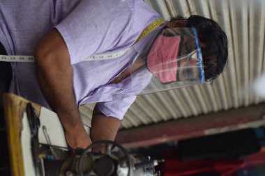 Hyderabad, Telangana, Hindistan. Temmuz-19-2020: terzi koruyucu yüz maskesi takarken giysileri tamir etmek, dikmek ve ayarlamak içindir. Yüzünde güvenlik maskesi olan bir adam, salgın konsepti.